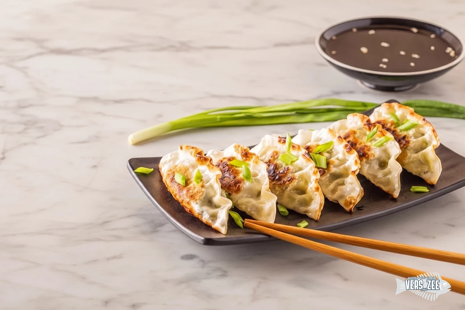 Gebakken gyoza (Japanse dumplings) gegarneerd met bosui op een rechthoekig bord, met eetstokjes, groene ui en een kommetje sojasaus op een lichte marmeren ondergrond.